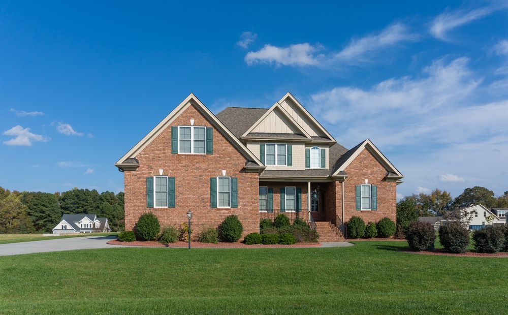 Brick two-story house with green shutters, lawn, and blue sky.