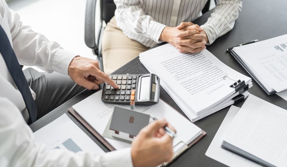 Person pointing at a calculator while reviewing documents with another person at a table.