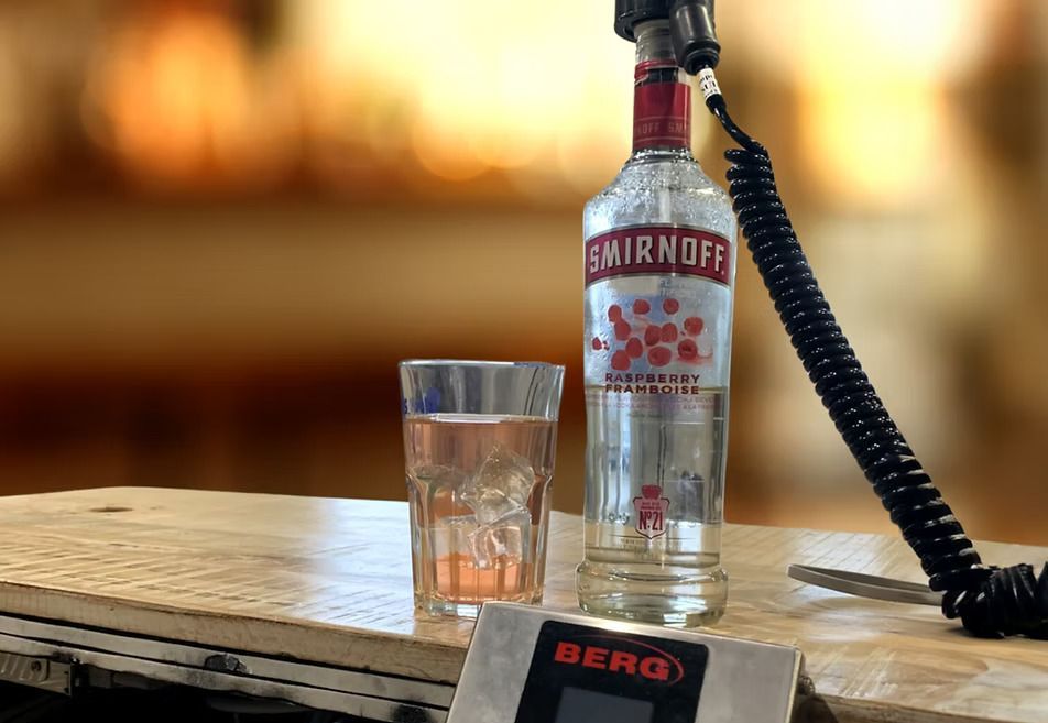 A bottle of smirnoff vodka next to a glass on a scale.