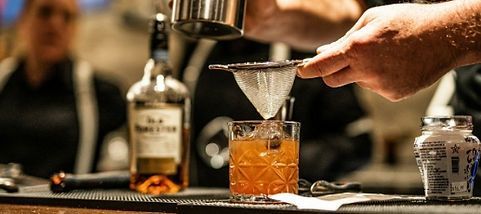 A bartender is pouring a drink into a glass with ice.