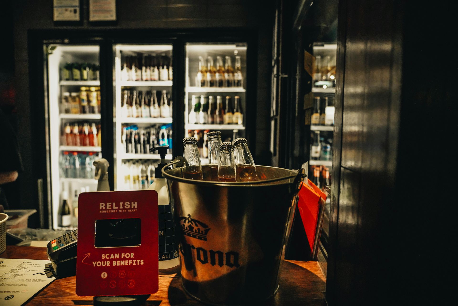 A bucket of beer is sitting on a table in front of a refrigerator in a bar.