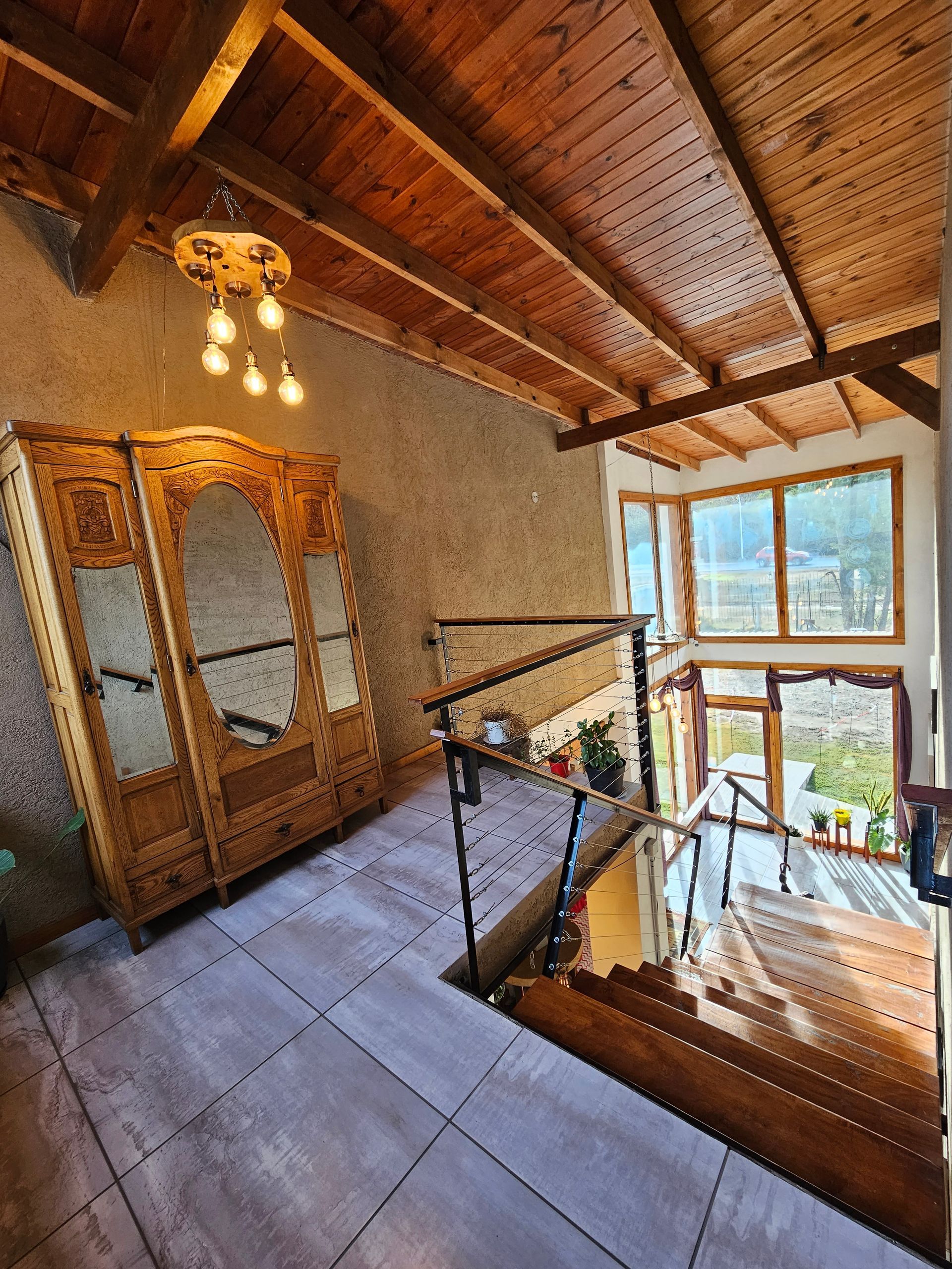 Wooden wardrobe and stairs in a room with a high, wood-beamed ceiling. Large windows offer a view.