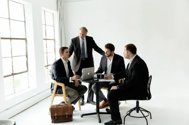 Business team meeting around a laptop in a bright office with large windows