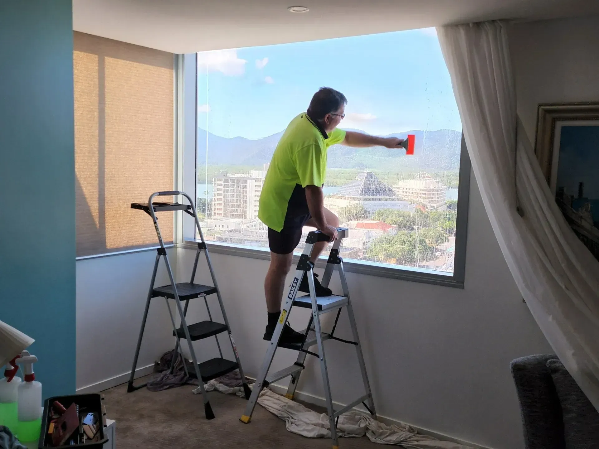 A Man is Standing on a Ladder Cleaning a Window — Ace Tinting in Mareeba, QLD