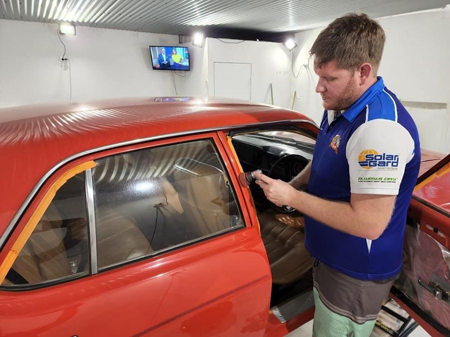 A Man in a Blue Shirt is Working on a Red Car — Ace Tinting in Mareeba, QLD