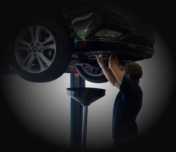 Mechanic inspecting the underside of a car lifted on a hydraulic lift in a dim garage | Integrated Automotive Services