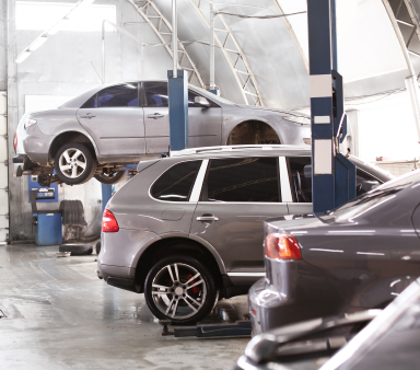 Cars in an auto repair shop, one lifted on a hydraulic lift and others parked below. | Integrated Automotive Services
