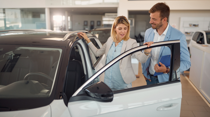 Salesperson showing a white car to a smiling customer in a showroom | Integrated Automotive Services
