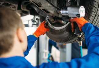 Mechanic in blue coveralls and orange gloves inspecting a car’s undercarriage in a garage | Integrated Automotive Services
