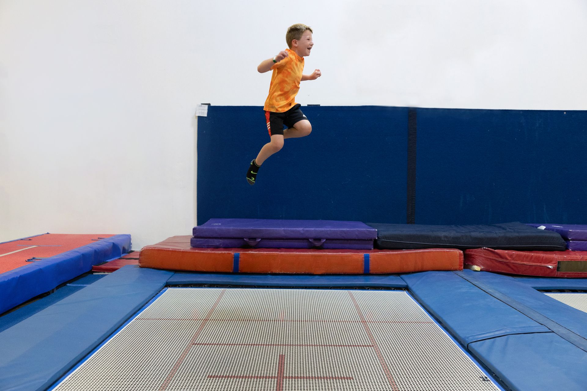 Child jumping on a trampoline in a gym with blue padded walls and mats