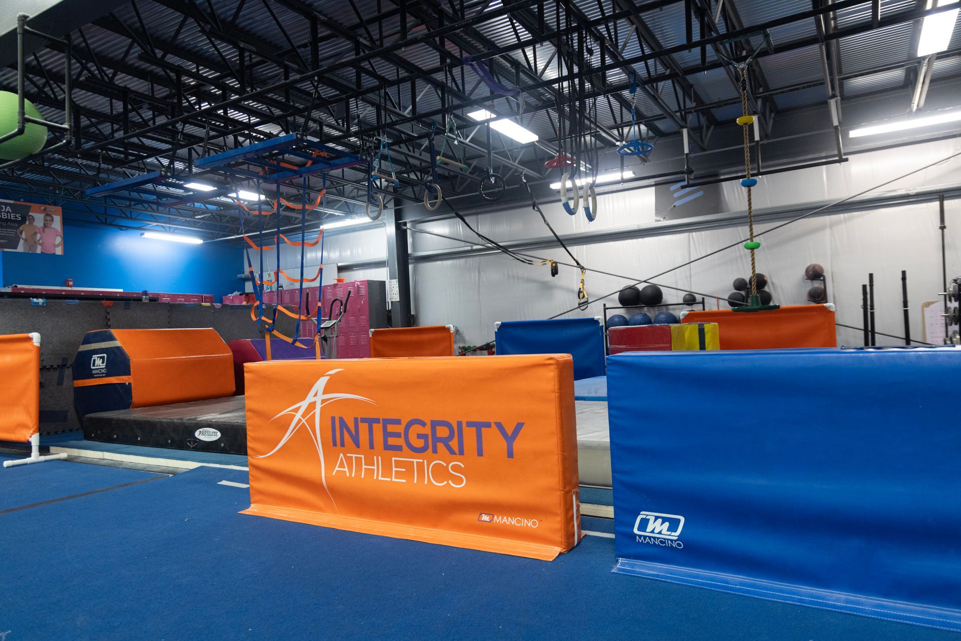 Indoor obstacle course gym with blue mats and orange barriers under high ceilings