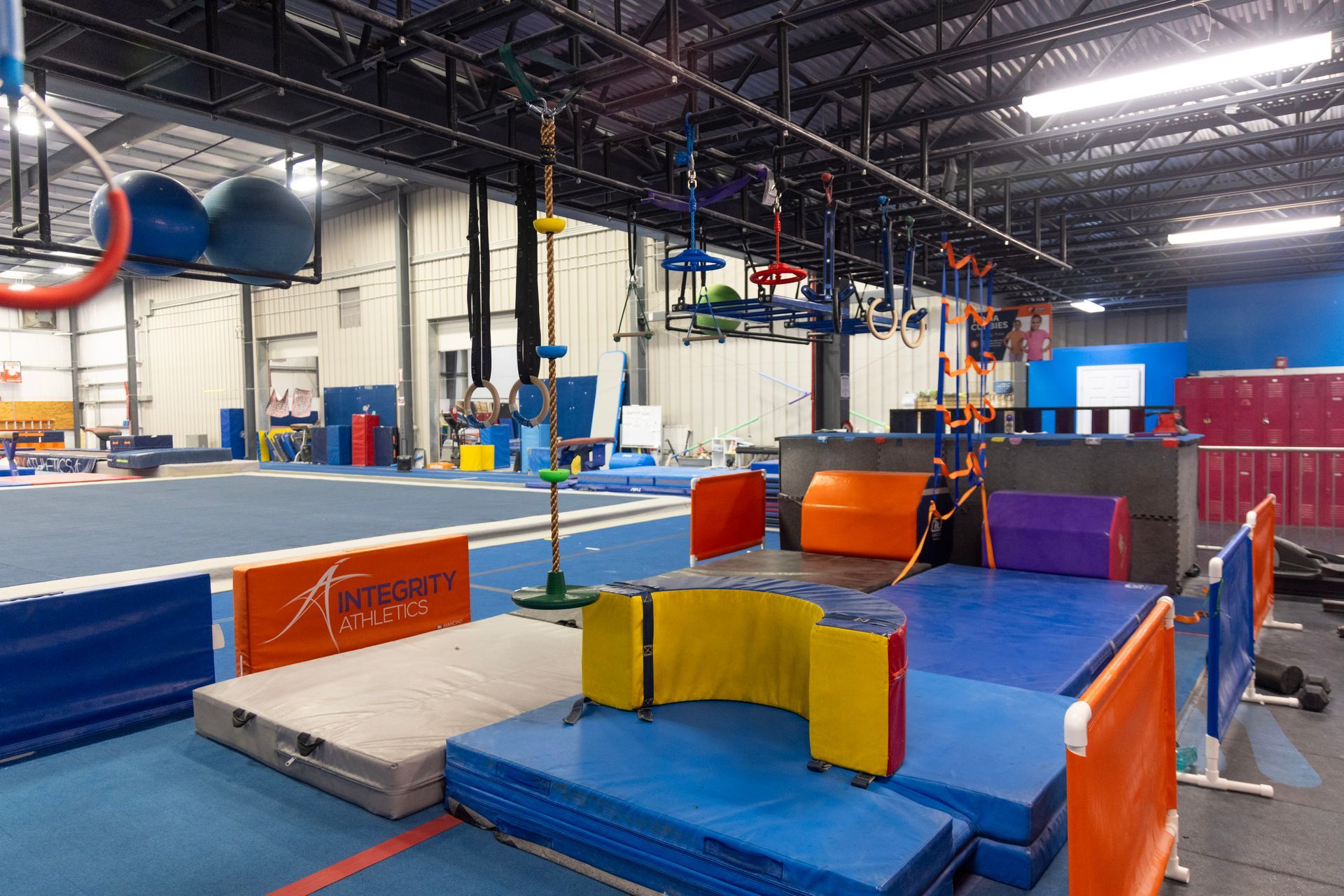 Indoor gymnastics training area with padded obstacle course, mats, and foam blocks under warehouse lighting