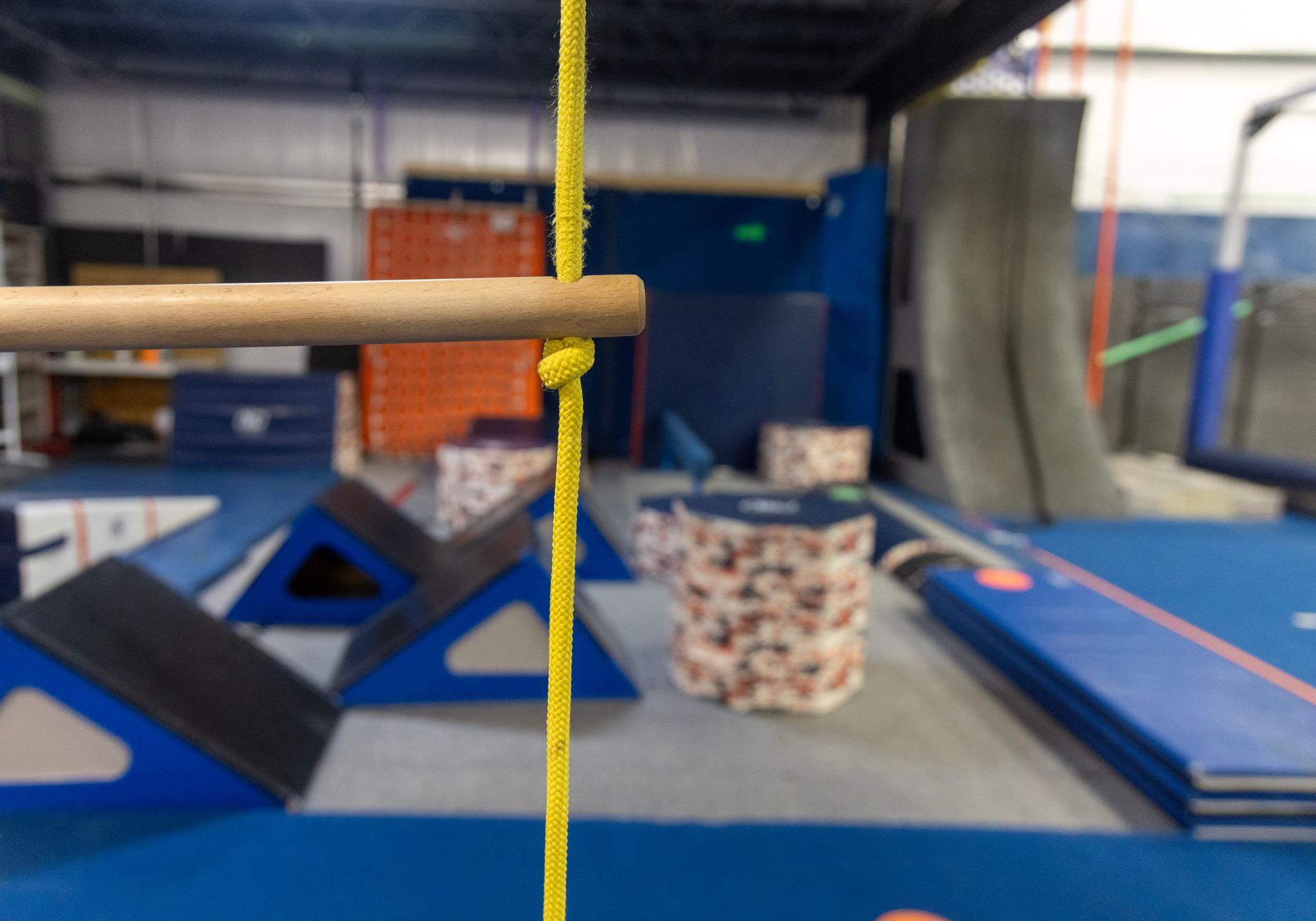 Indoor gym with blue mats, obstacle course equipment, and a yellow rope in the foreground.