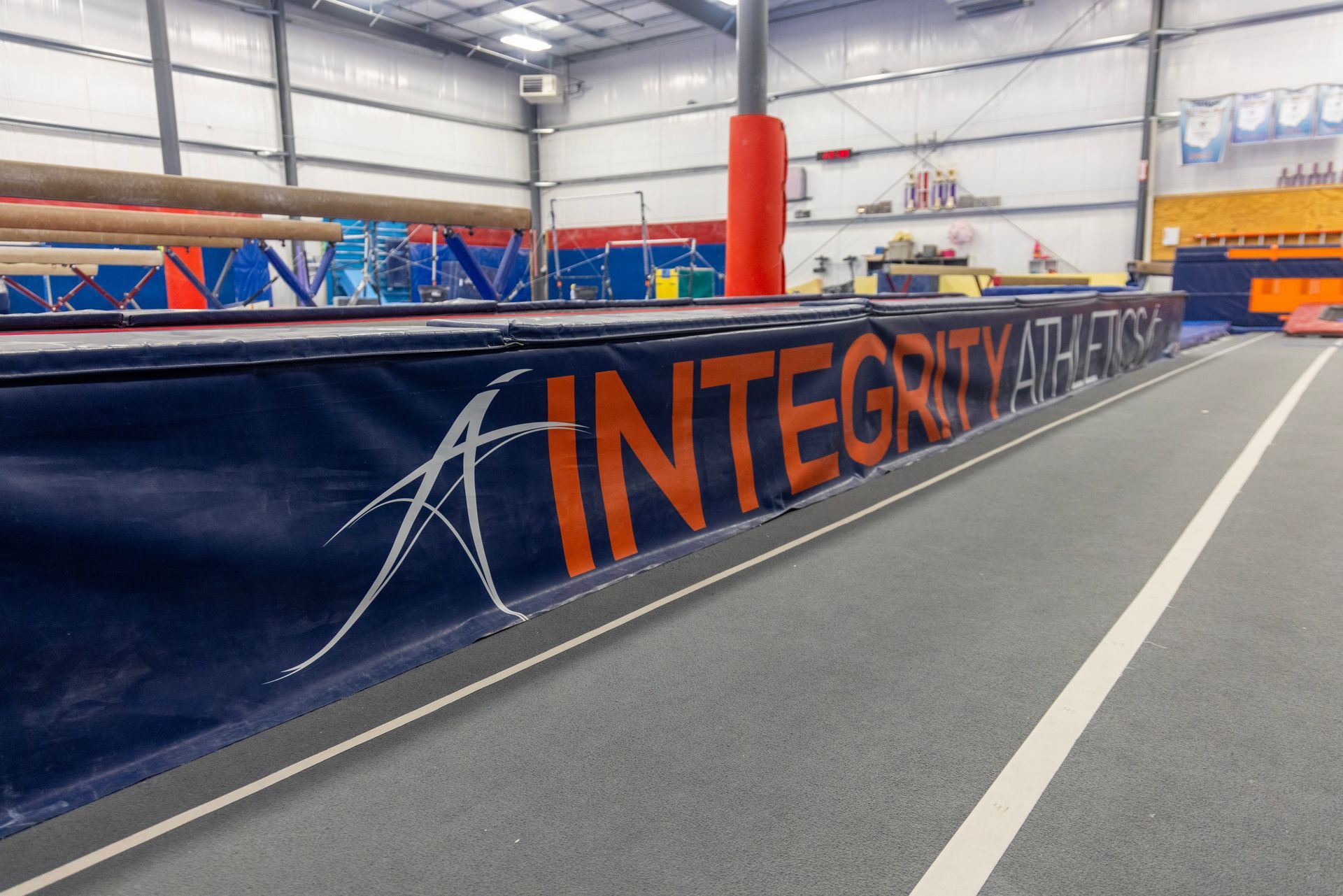 Indoor sports arena with a blue barrier labeled “INTEGRITY,” beside a running track and hurdles