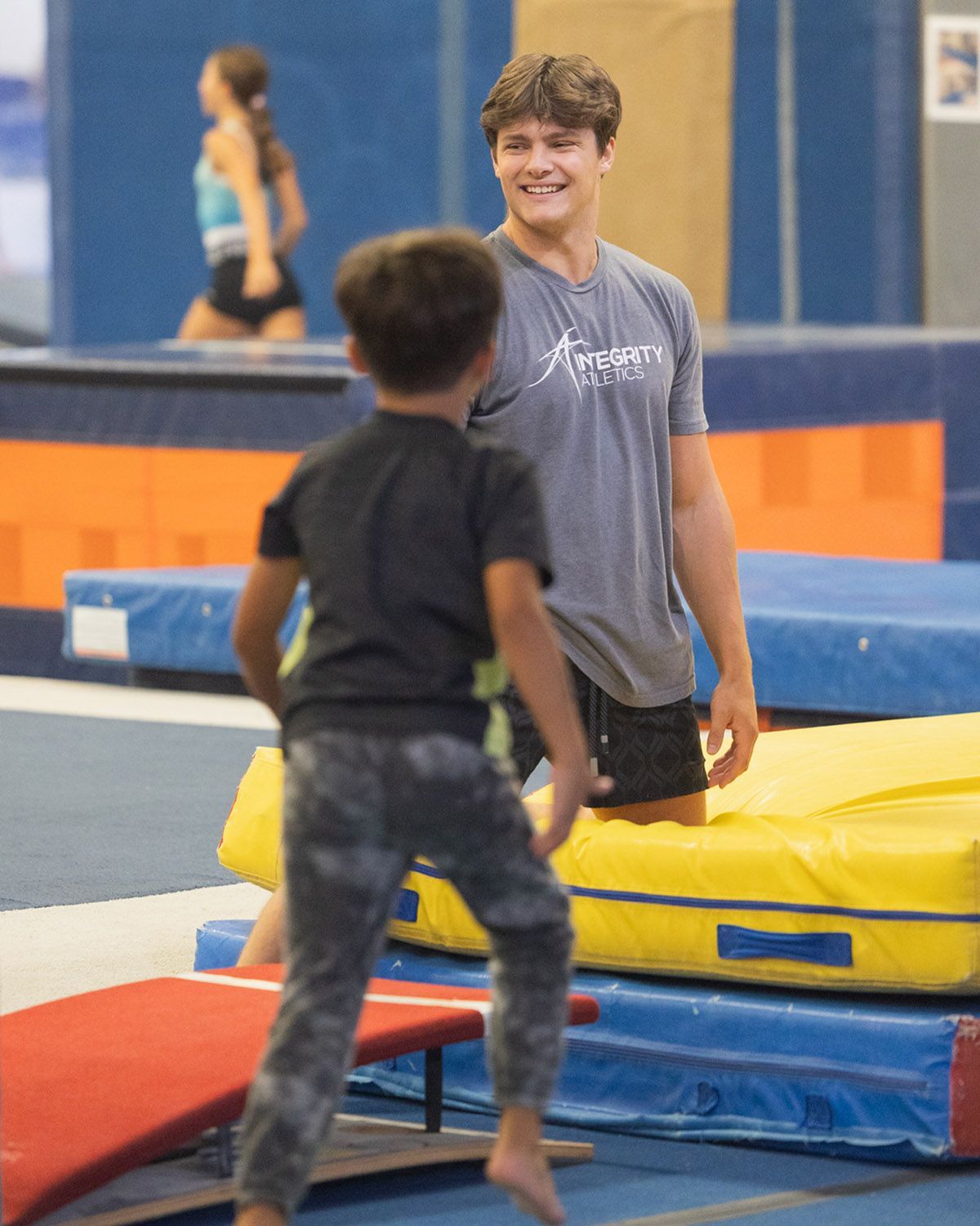 Two people bouncing on padded mats in a gym, with one smiling and facing the other.