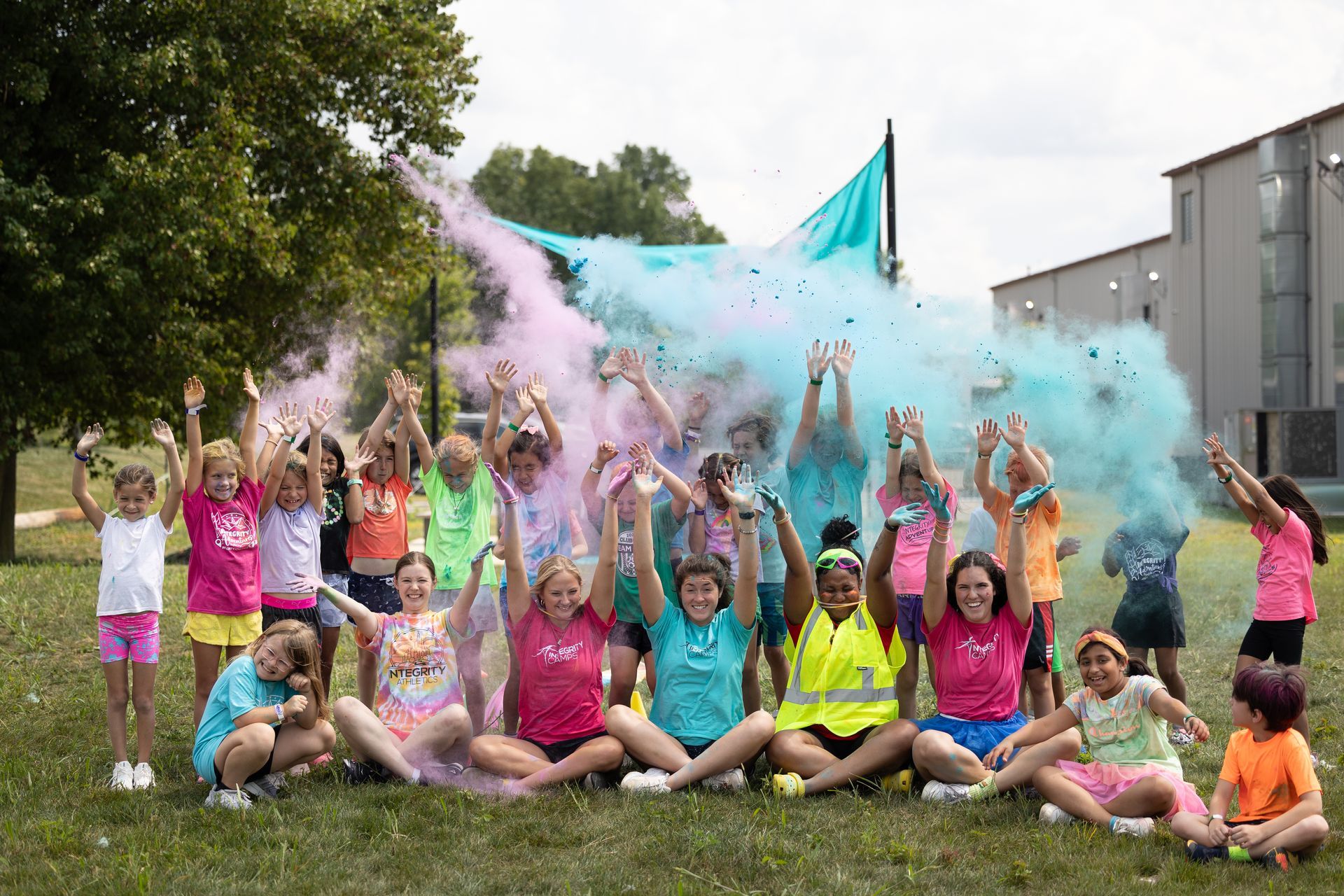 Group of children tossing colorful powder in a grassy outdoor celebration