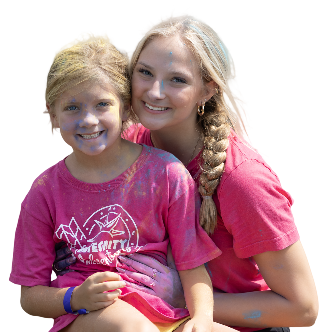 Two smiling children in bright pink shirts sitting close together outdoors