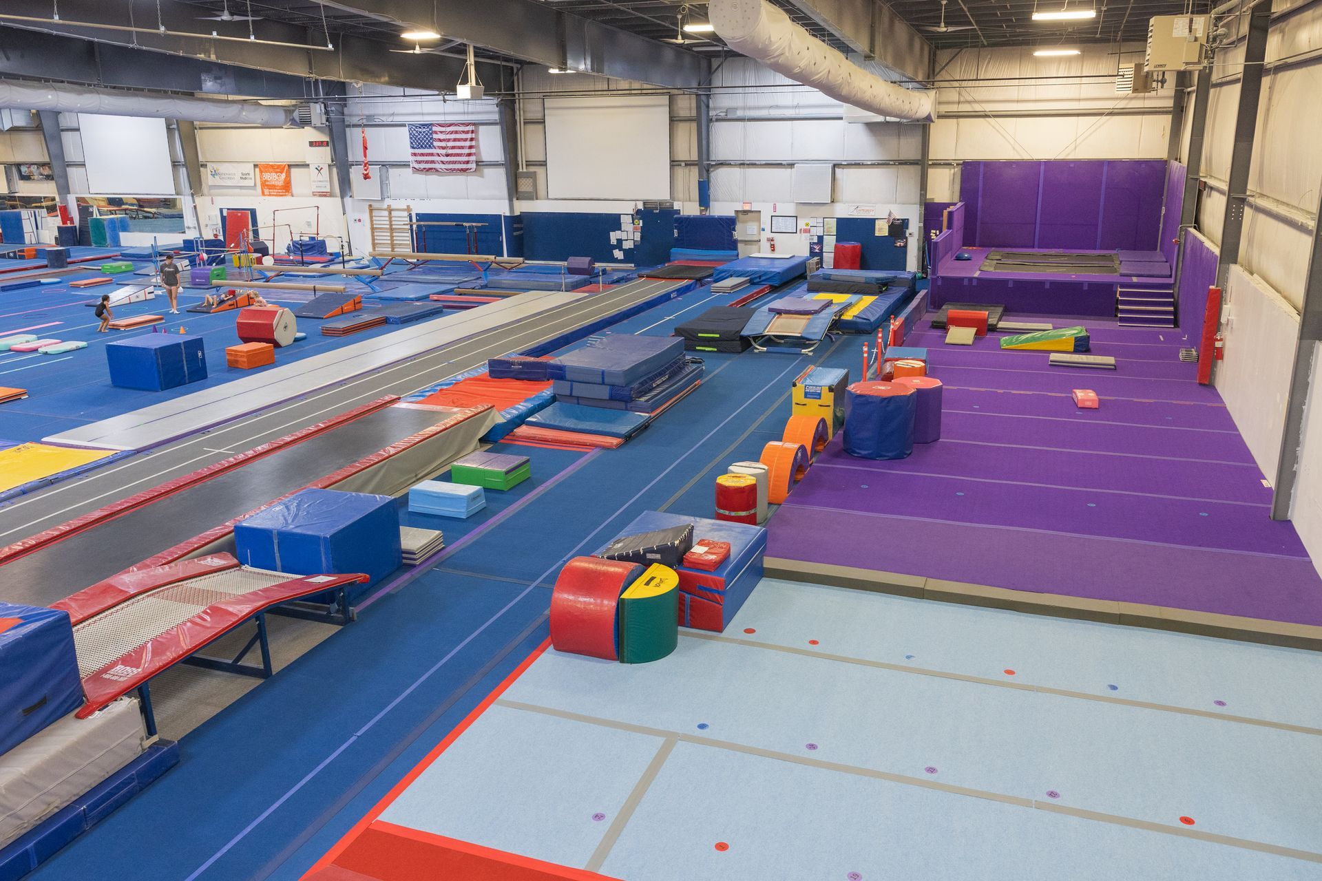 Indoor trampoline park with blue and purple padded lanes and foam blocks under bright lights