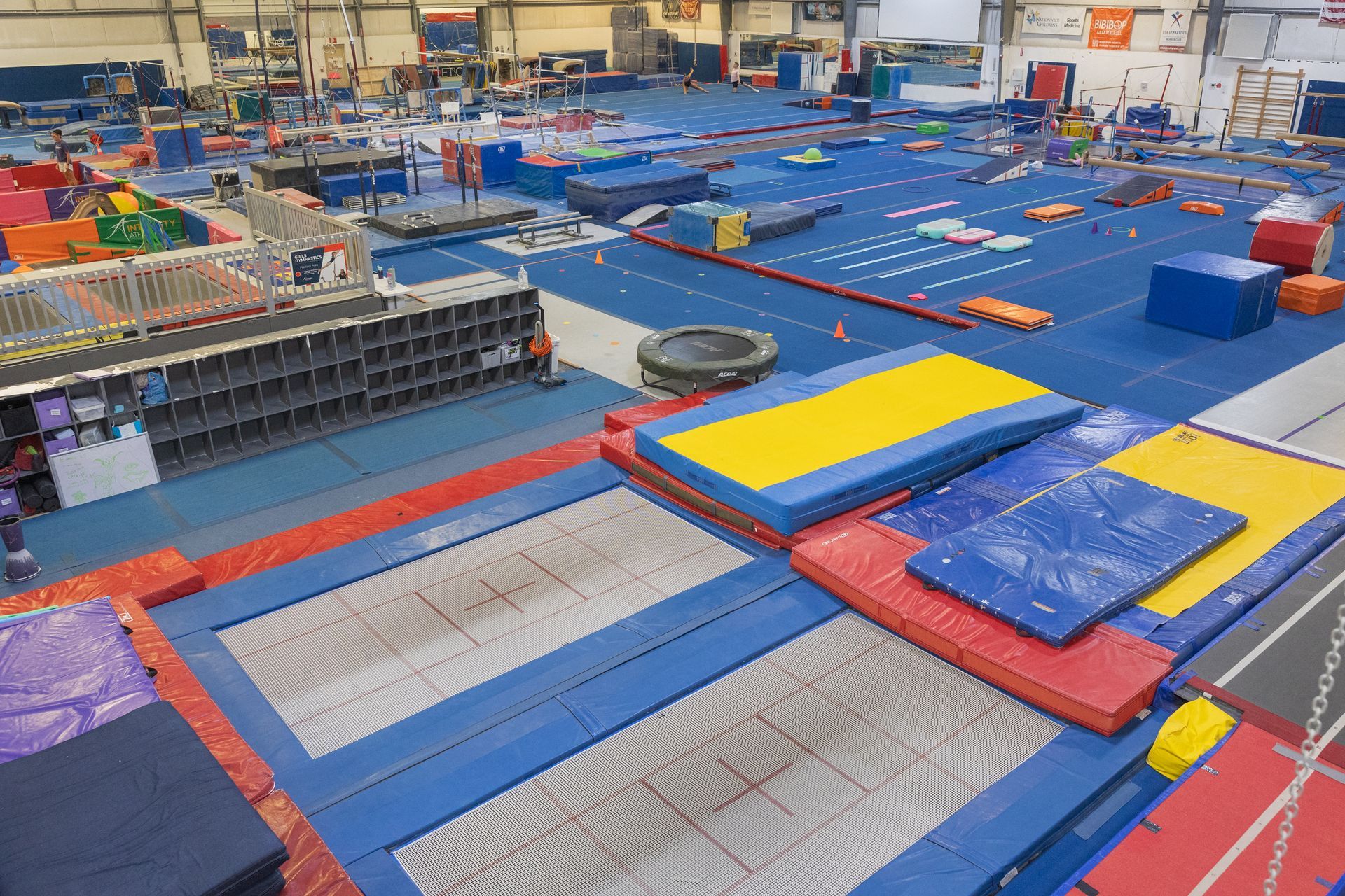 Indoor gymnastics training area with blue mats, red borders, and yellow foam blocks on a large floor.