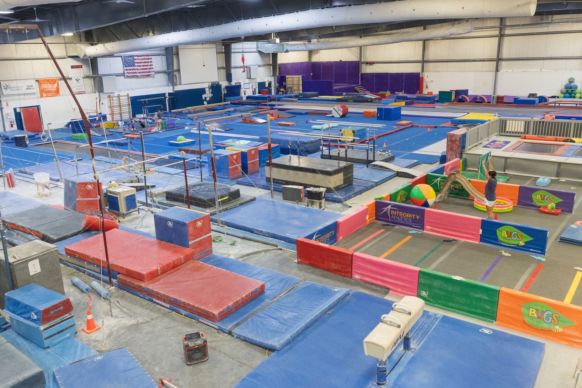 Indoor gymnastics gym with colorful mats, balance beams, trampolines, and foam blocks
