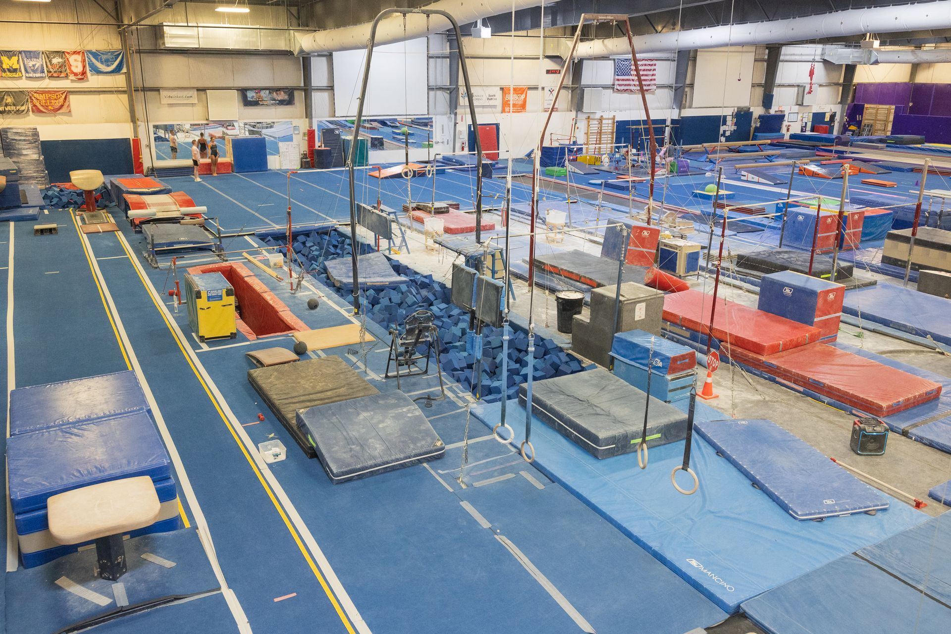Indoor gymnastics training facility with blue mats, balance beams, and padded equipment arranged across the floor