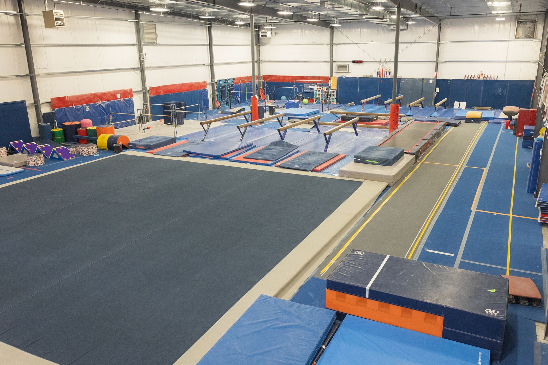 Indoor gymnastics training facility with blue mats, trampolines, and balance equipment