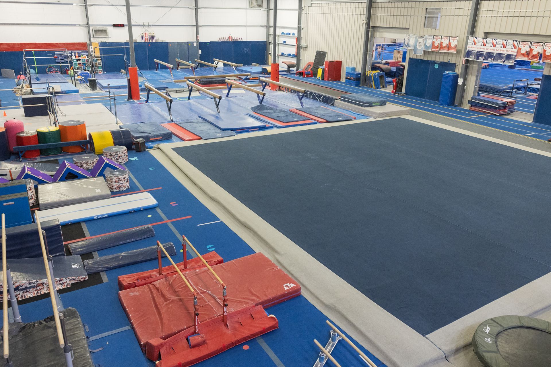 Gymnastics training facility with blue mats, balance beams, and a large floor exercise area