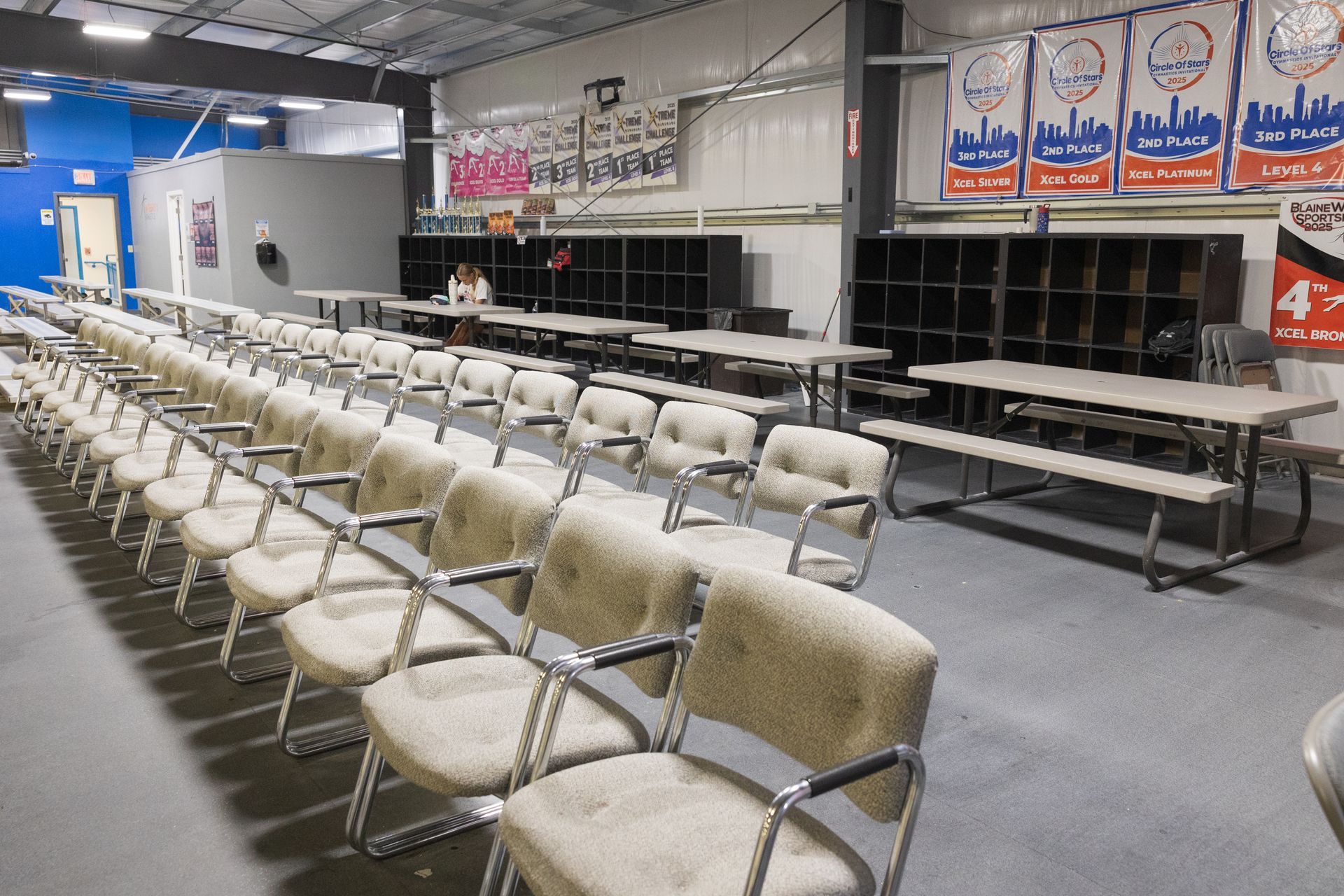 Empty waiting room with rows of beige chairs and tables under fluorescent lights