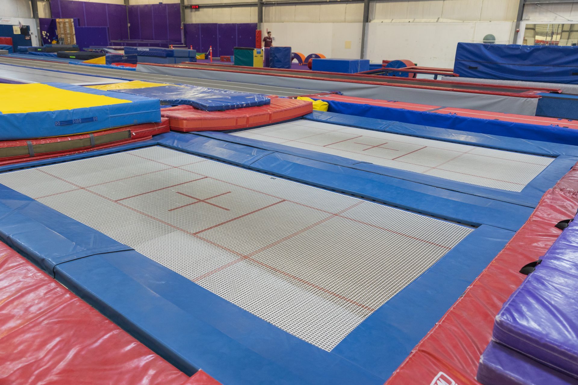 Indoor gymnastics trampoline area with blue, red, and white padded mats on the floor
