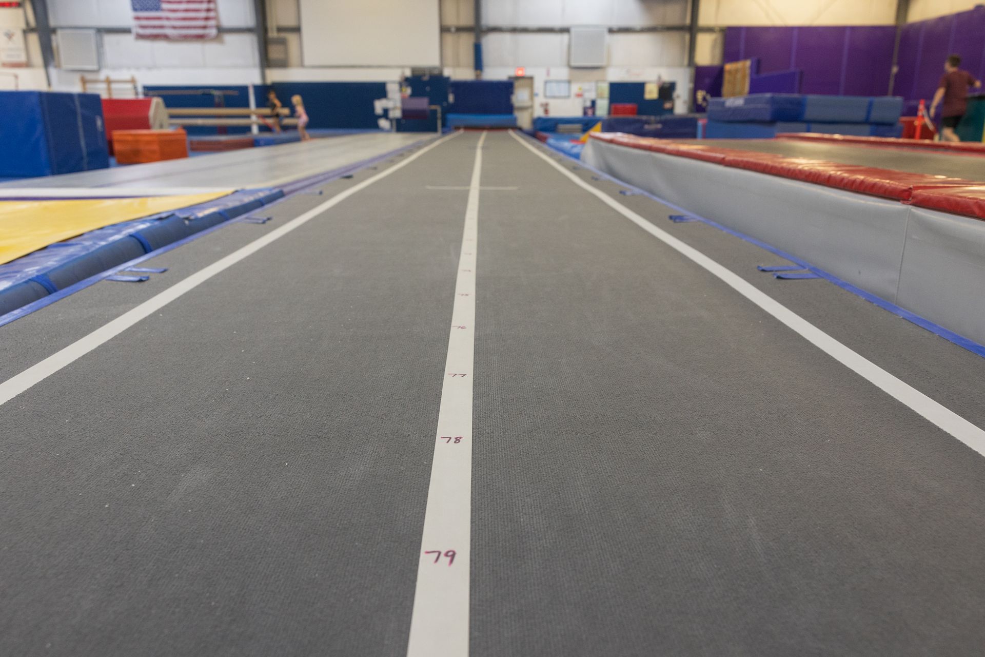 Indoor gymnastics runway with white center lines and blue and red mats on either side