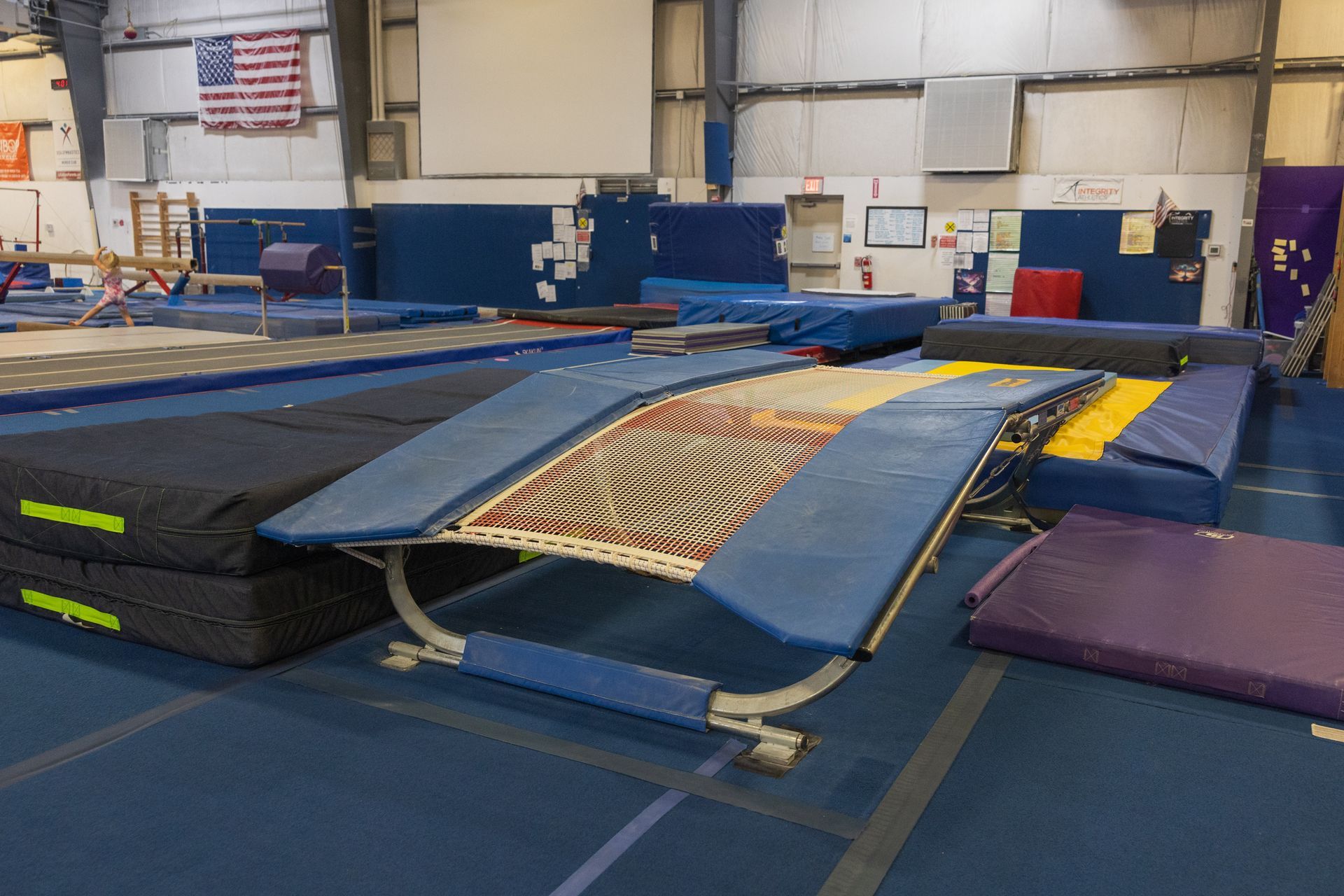 Gymnastics training pit with blue and yellow mats and a trampoline in an indoor gym
