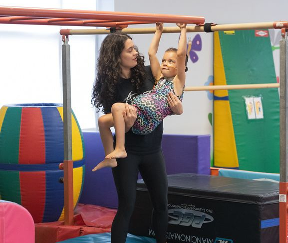 A child is standing on a balance beam in a gym.