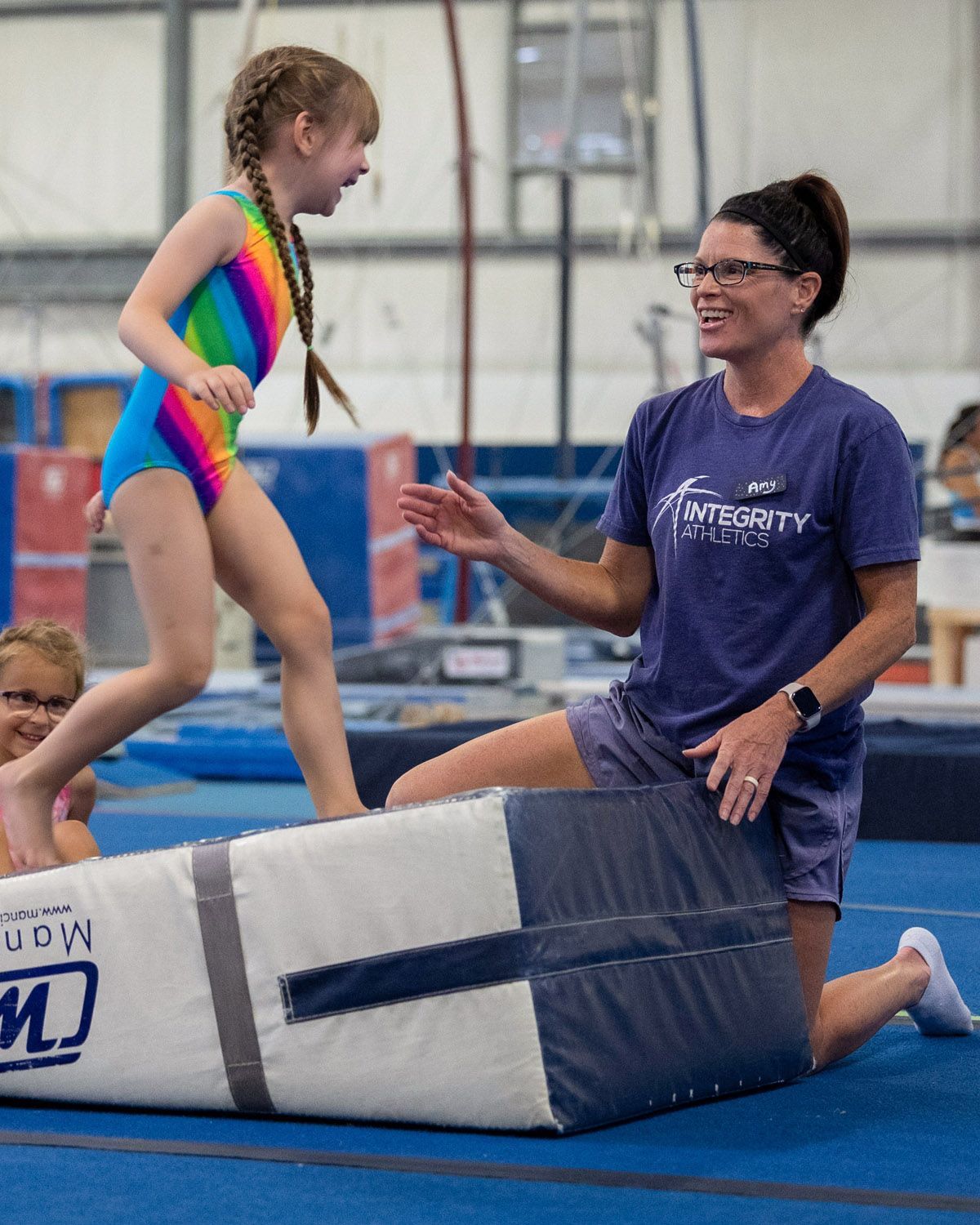 Coach helping child balance on gymnastics mat in indoor gym