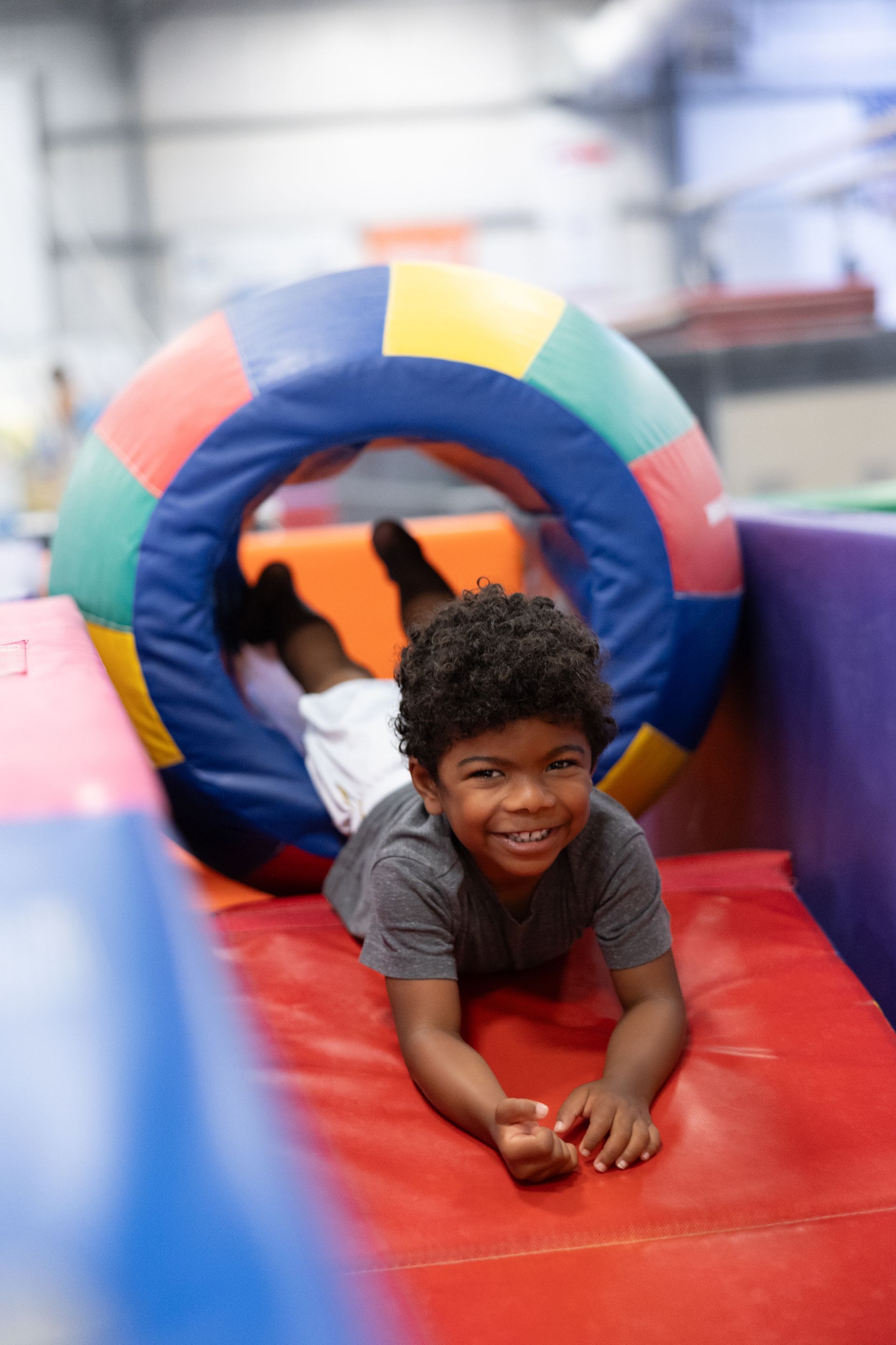 Child sliding on a colorful inflatable obstacle course, smiling toward the camera.