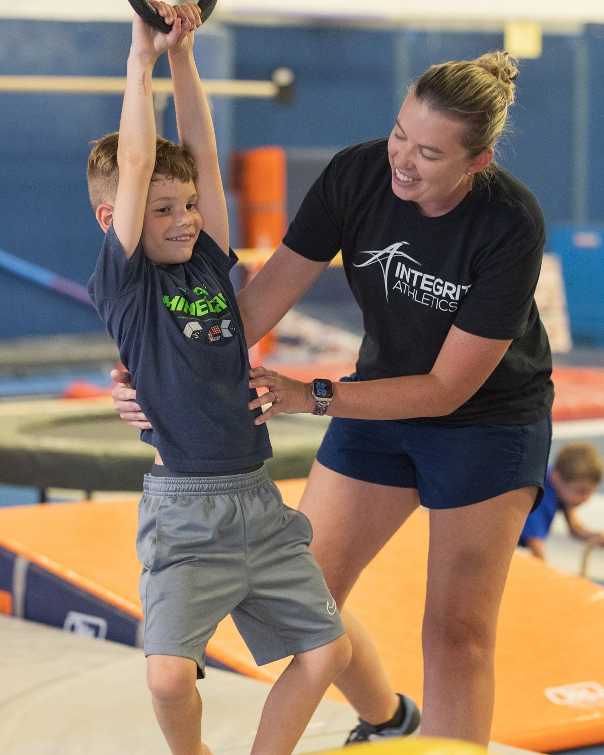 A man is helping a young girl do a handstand on a blue mat