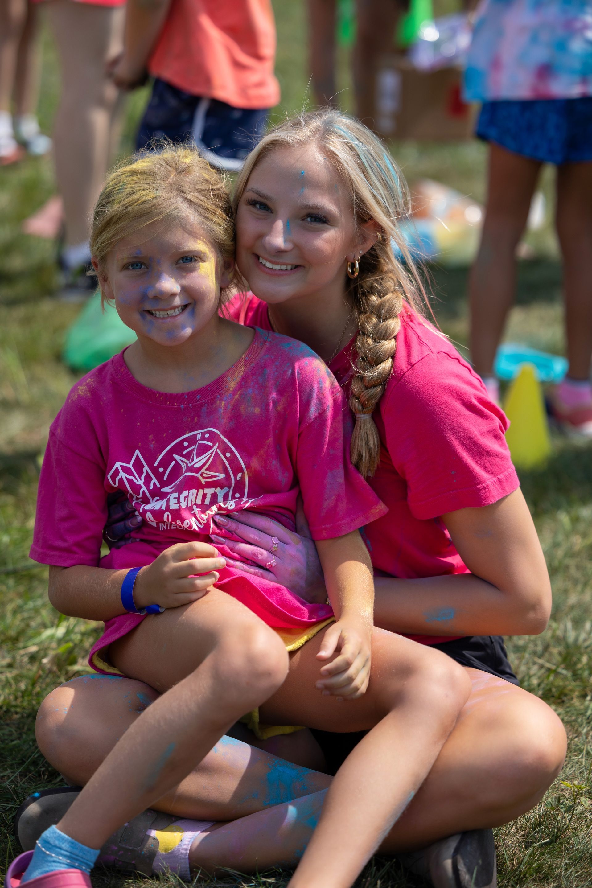 Two smiling girls in bright pink shirts sitting together outdoors at a group event