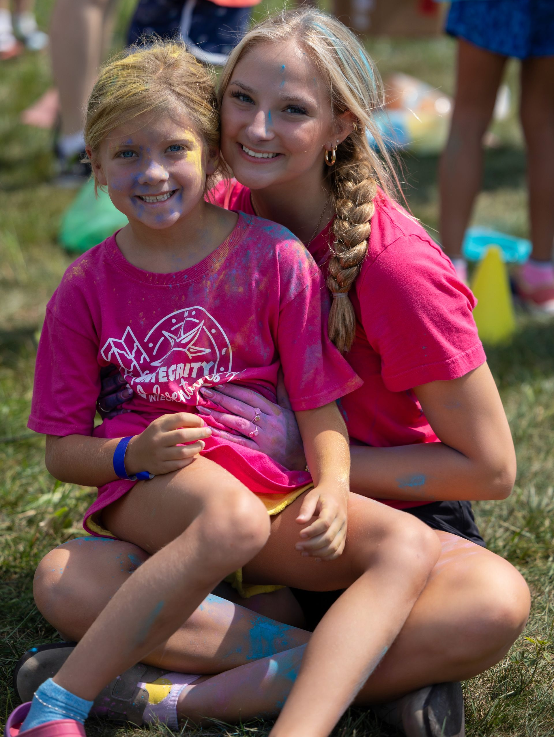 Two smiling children in bright pink shirts sitting together outdoors