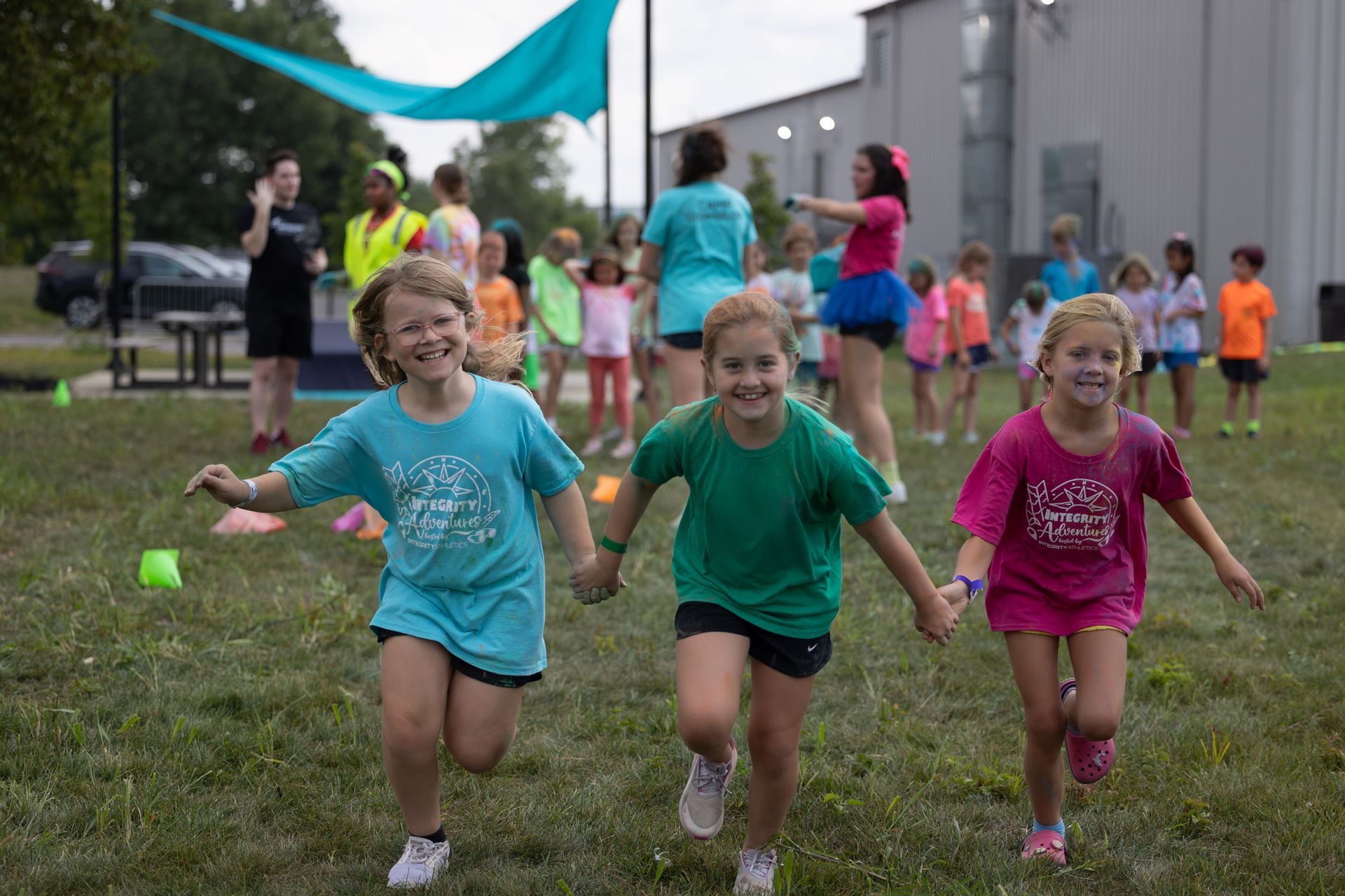 Three children running barefoot at a colorful outdoor race event on grass