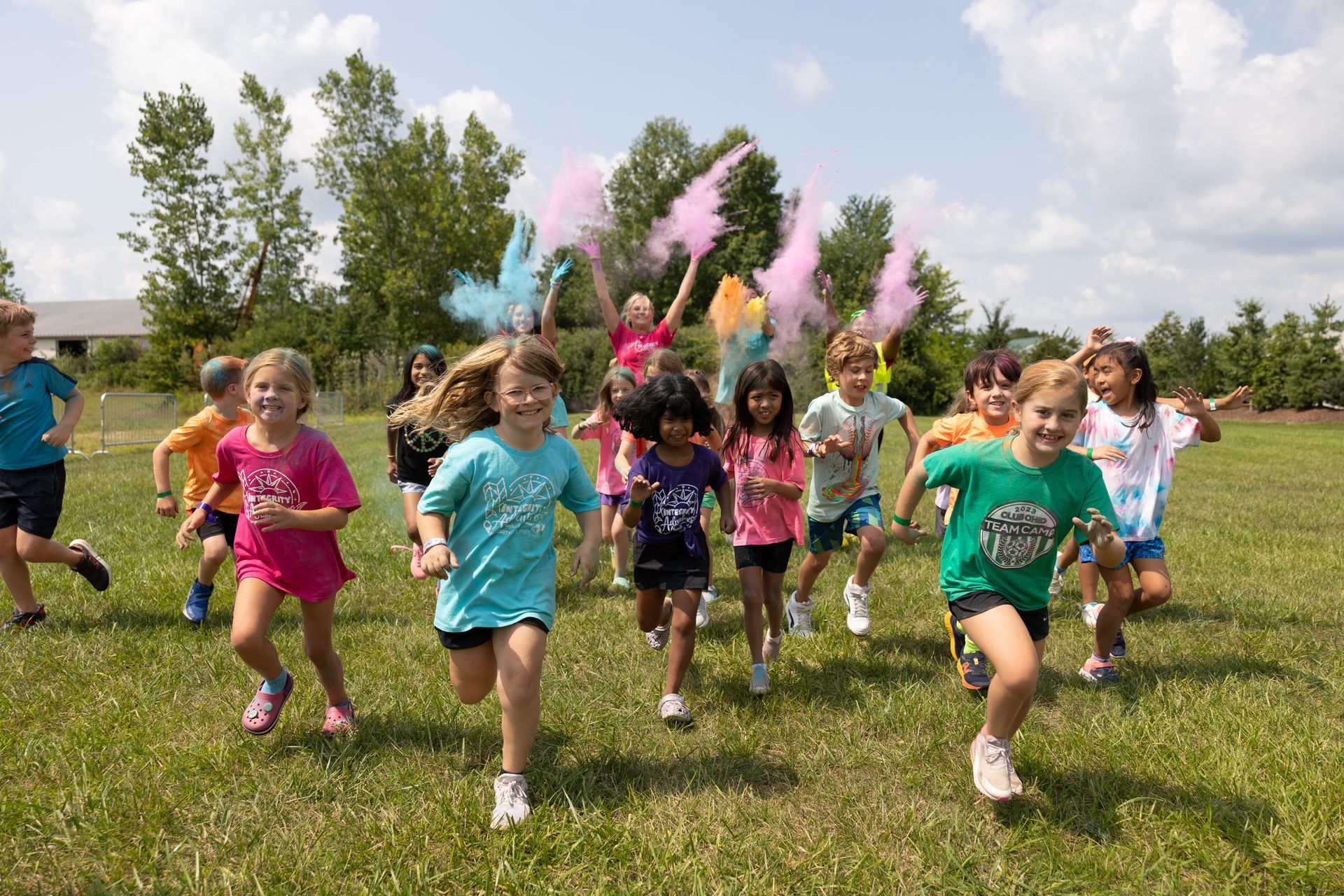 Children running through colored powder in a grassy field outdoors