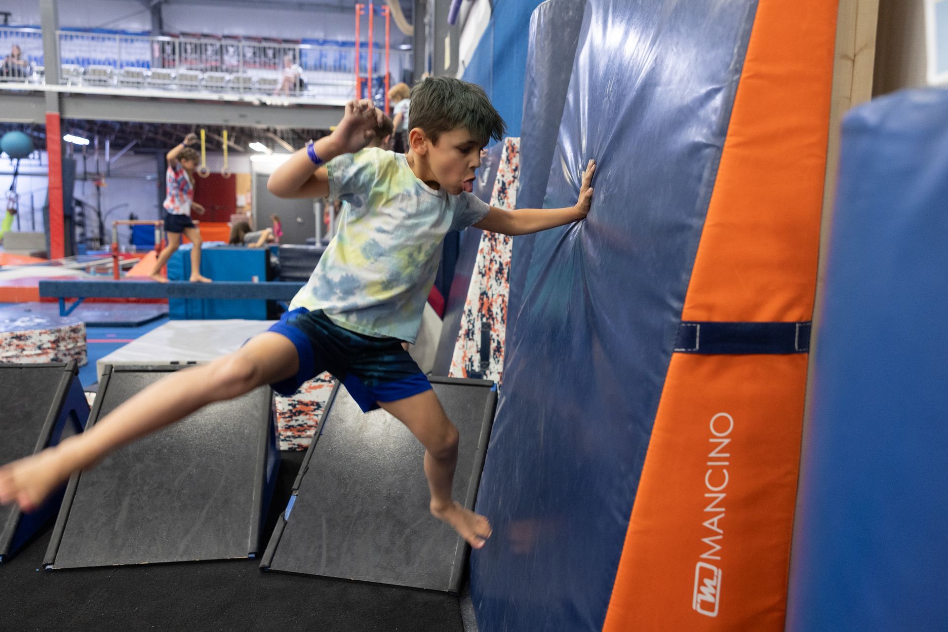 Child jumping onto a blue and orange inflatable obstacle in an indoor gym