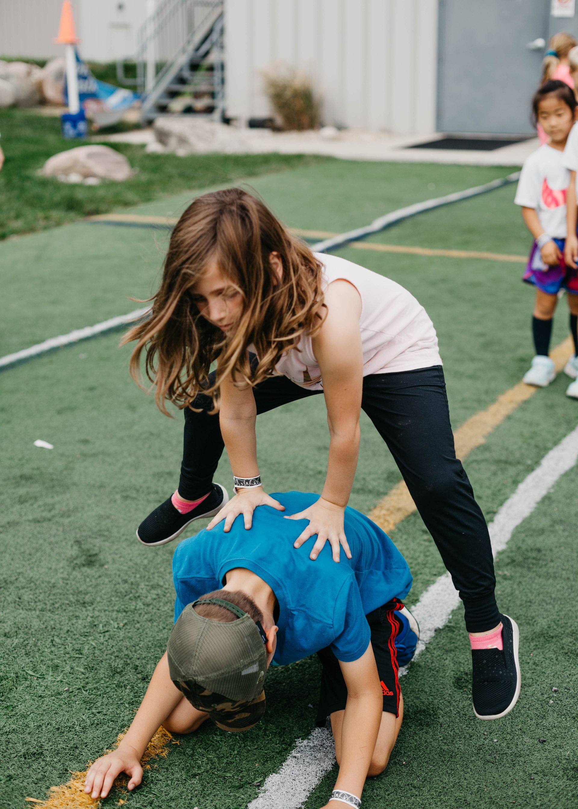 Child in white shirt and black pants on a sports field, with other kids nearby