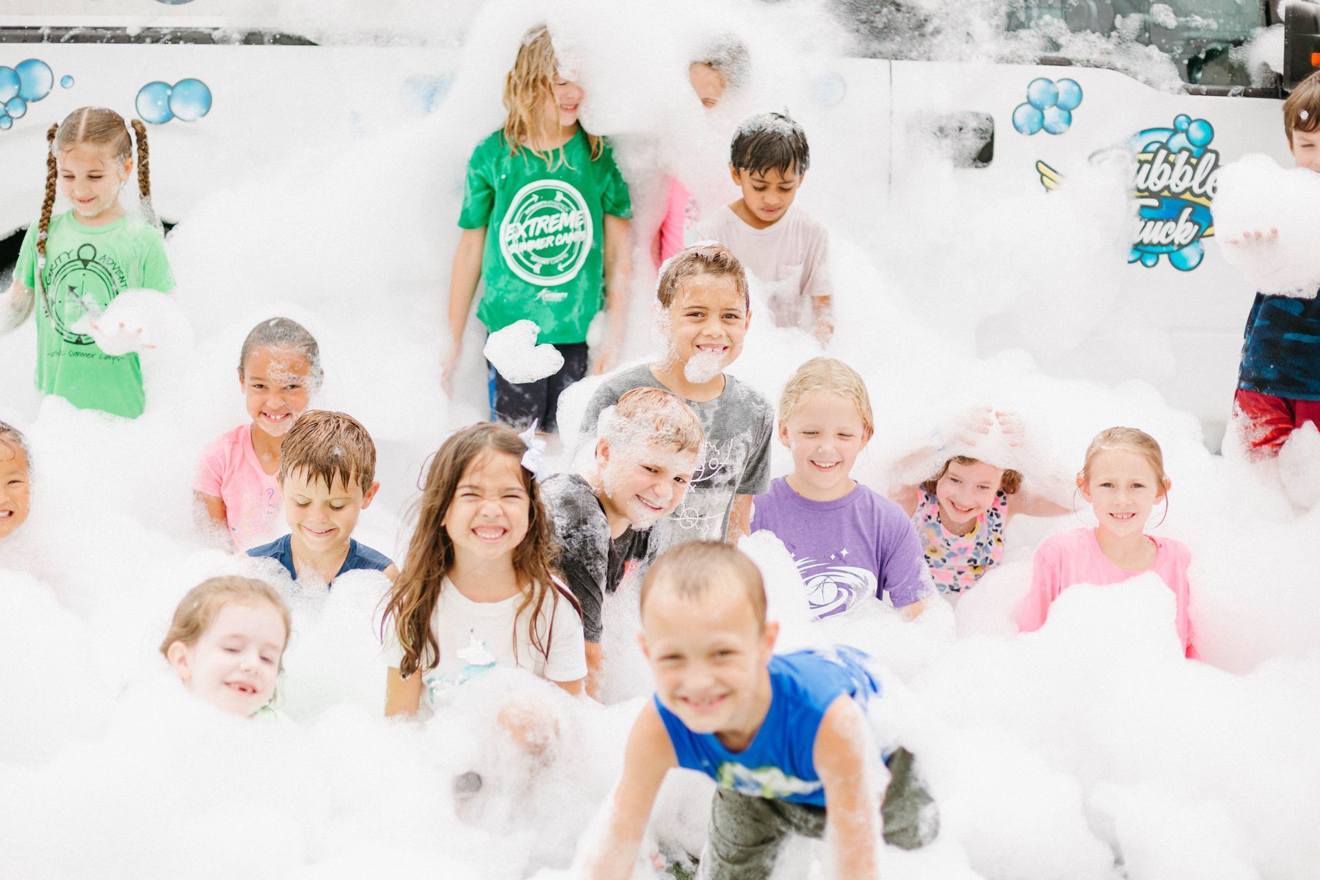 Children playing in a white foam pit, smiling and covered in bubbles.