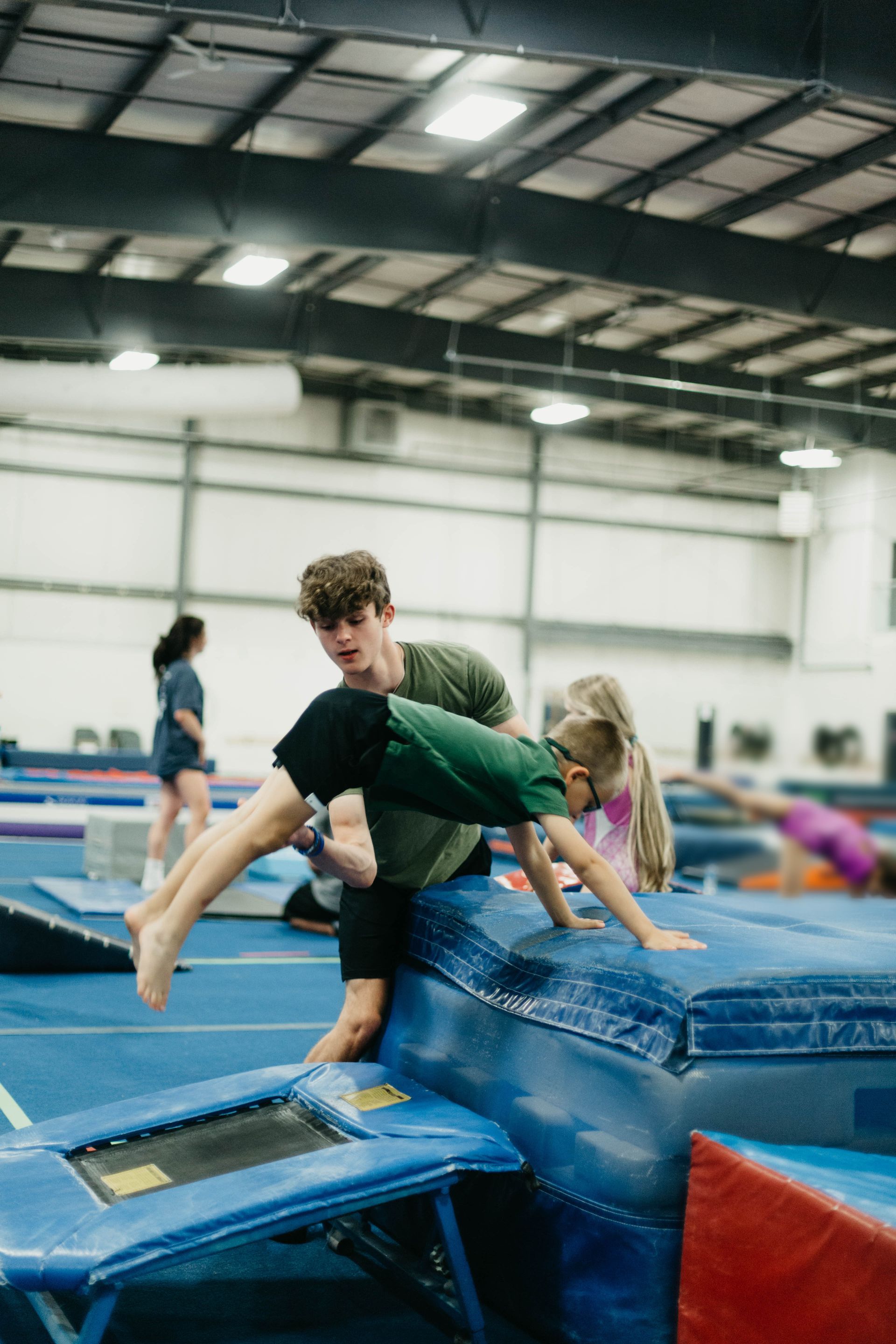 Gymnast balancing on blue foam blocks in an indoor gymnastics gym with mats and equipment.