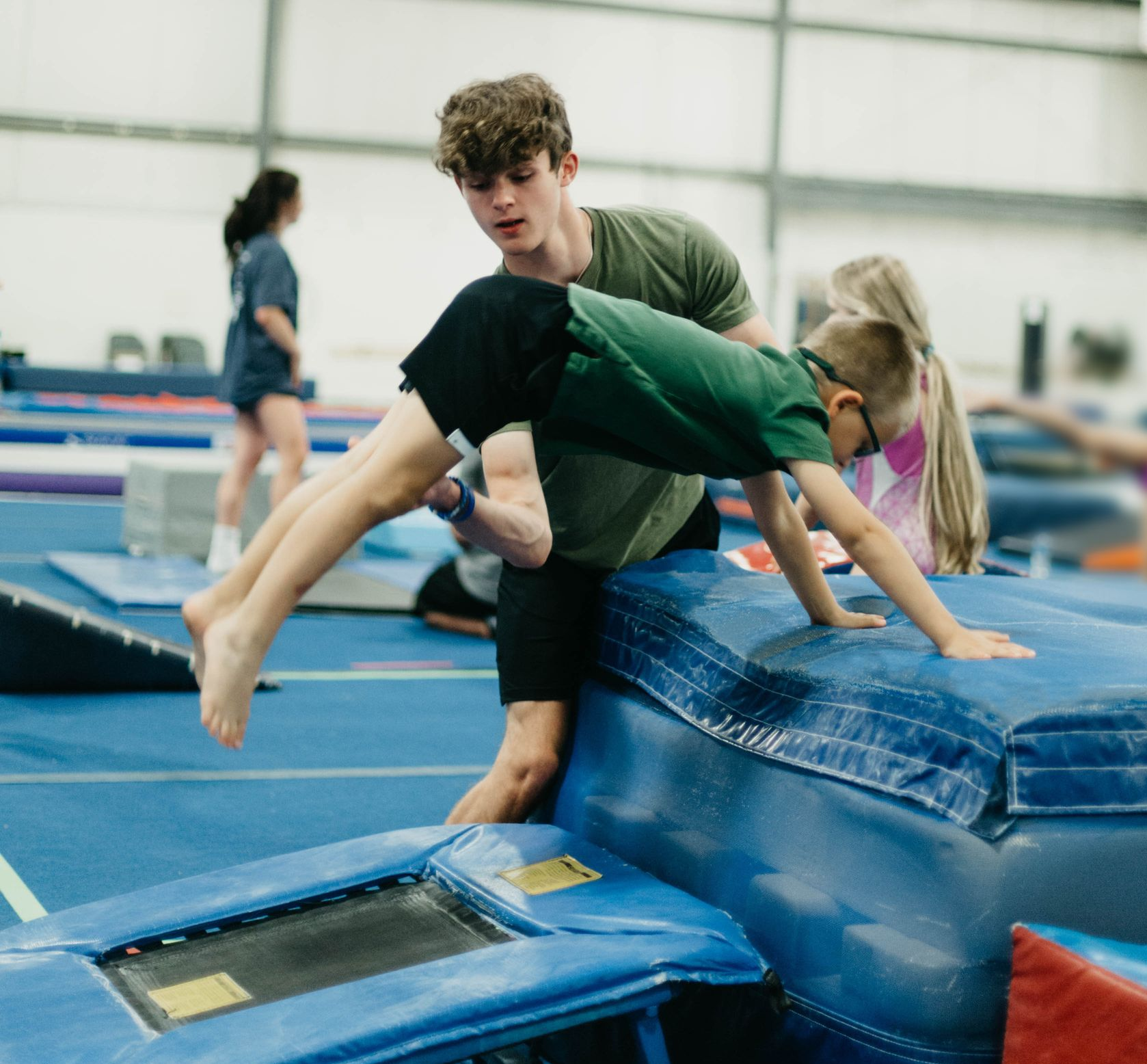A woman in a purple shirt is helping a little girl on a balance beam.