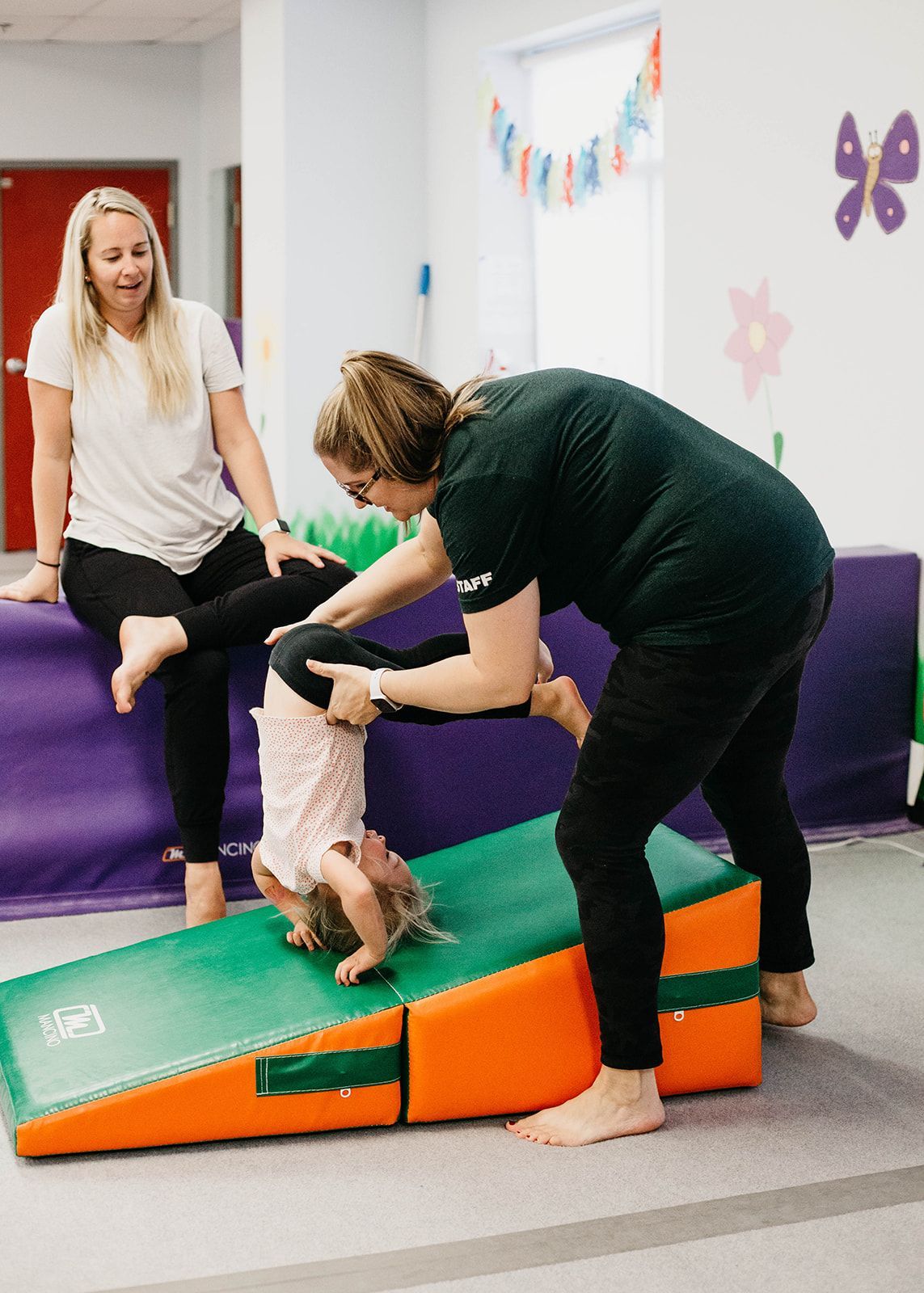 Instructor helping child on colorful foam gym equipment in a playroom