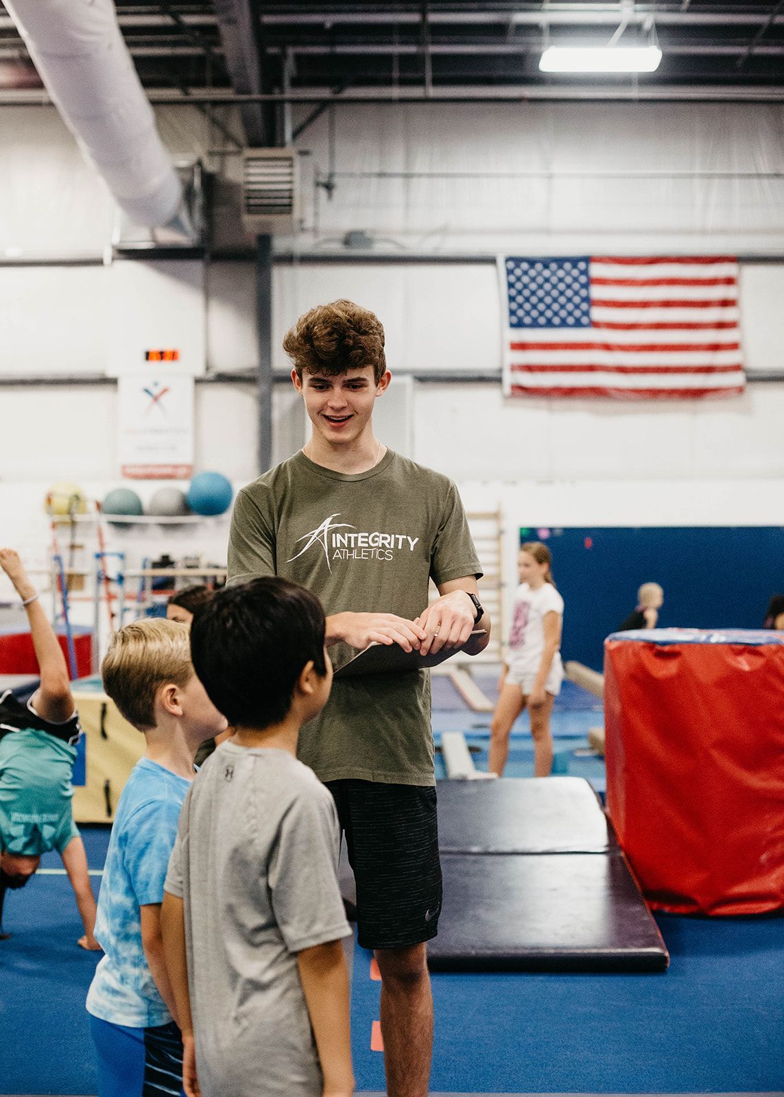 Gymnastics coach handing out chalk to children in a gym with an American flag in the background