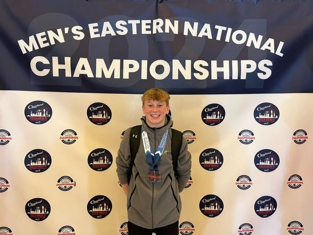 Person wearing a medal stands in front of a Men's Eastern National Championships backdrop.