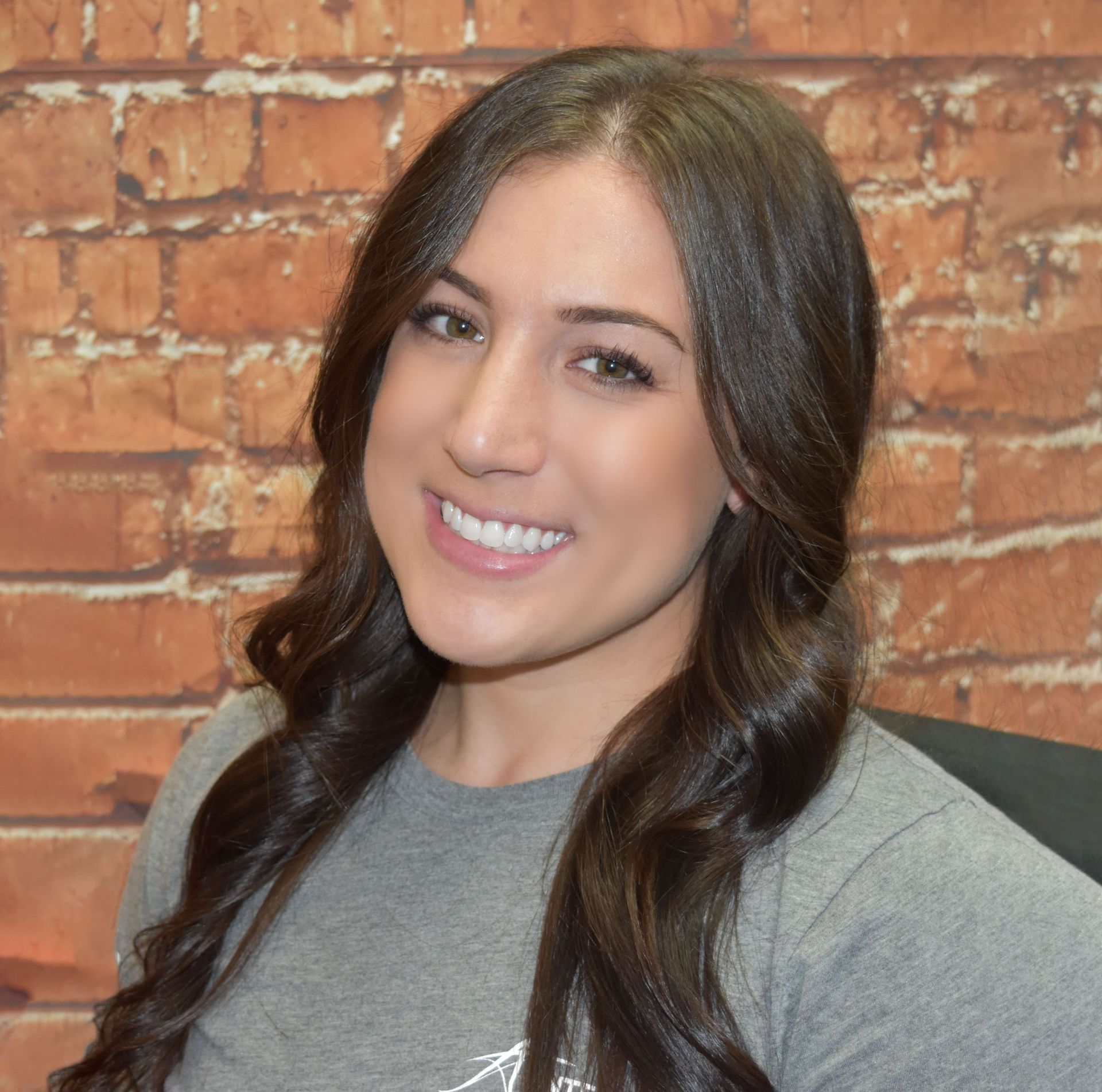 Smiling woman with long dark hair in front of a brick wall