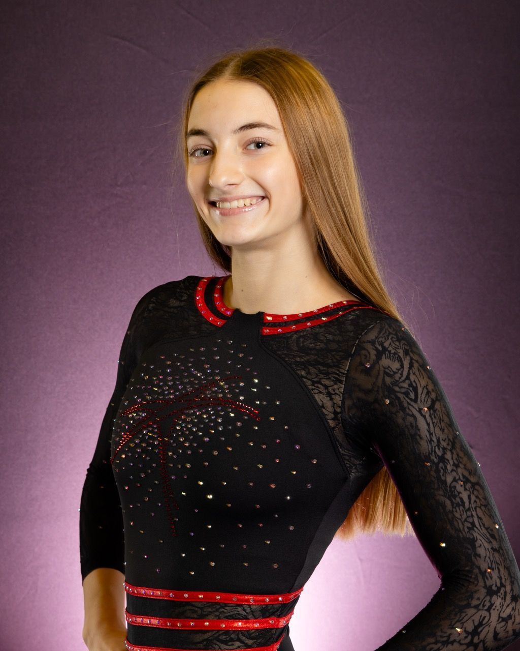 Person smiling in a black lace dress with red accents against a purple backdrop