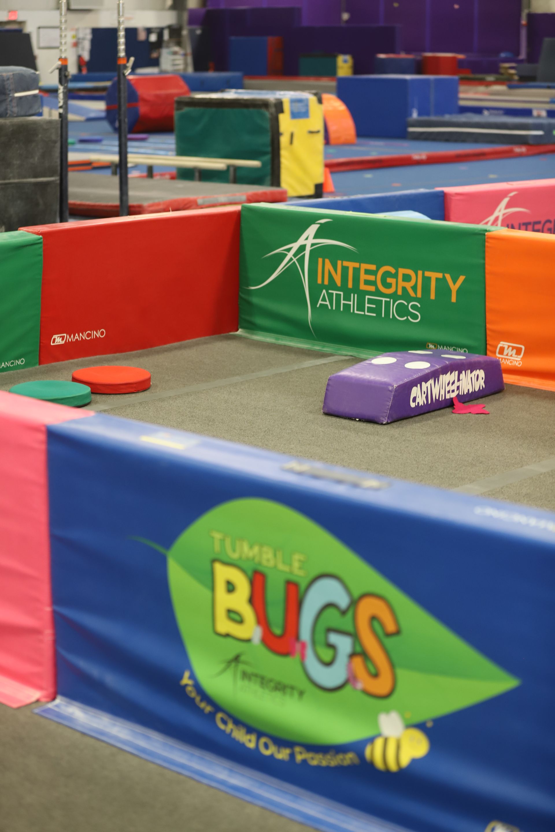 Indoor mini-golf course with colorful bumpers and sponsor signs, including “Integrity” and “Tumble Bugs” banners